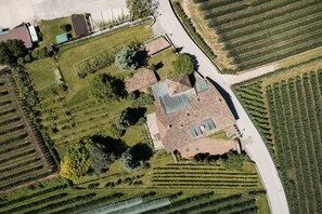 Eine Vogelperspektive zeigt ein Anwesen mit einem zentralen Gebäude, umgeben von angelegten Gärten und Weinreben.