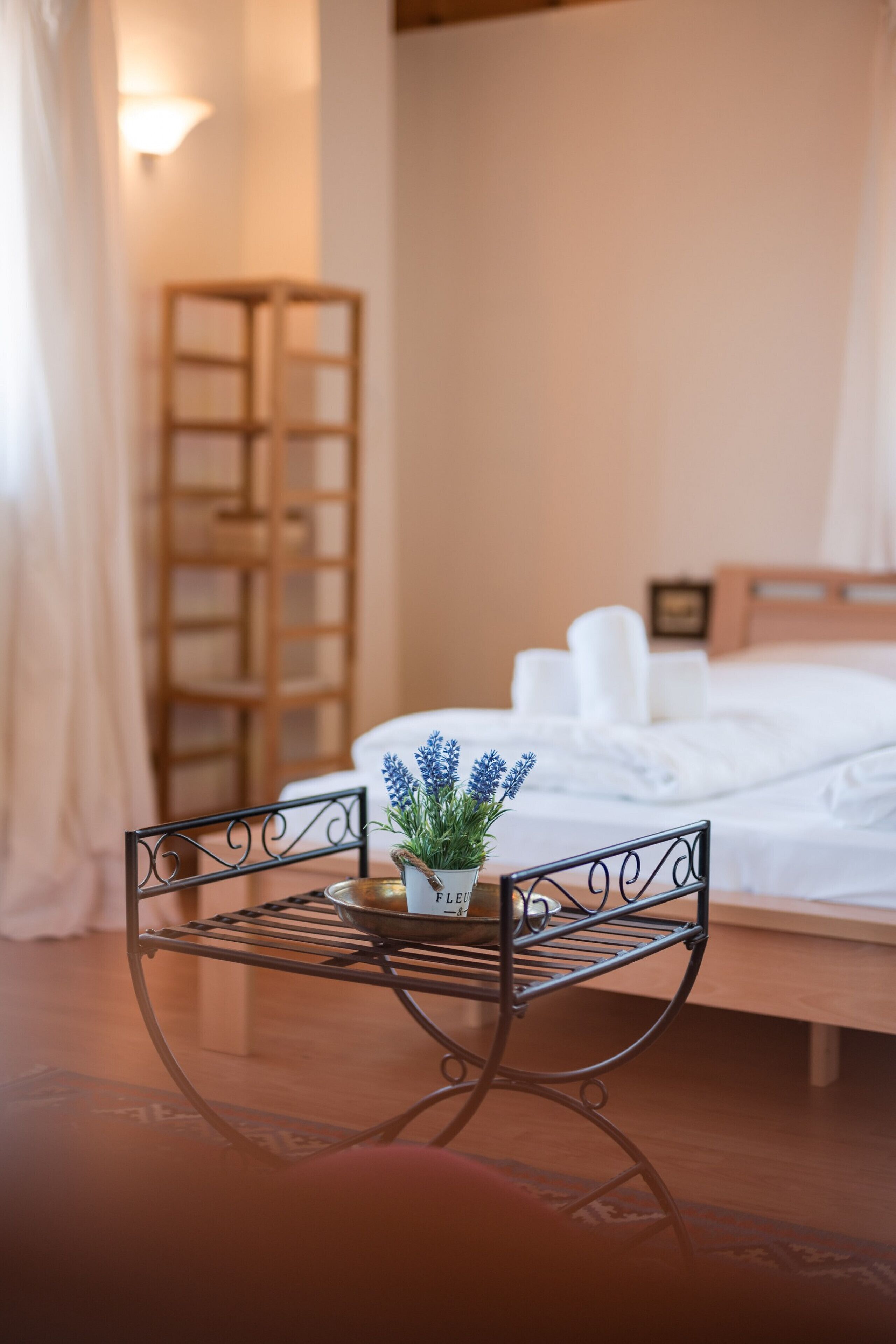 Une chambre d’hôtel avec un lit, une petite table sur laquelle est posée une plante en pot, une chaise en métal et une échelle en bois appuyée contre le mur.