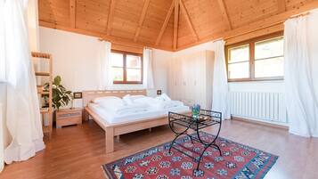 Un dormitorio con techo de madera, una cama, una mesita de noche, cortinas en una ventana y una alfombra estampada.