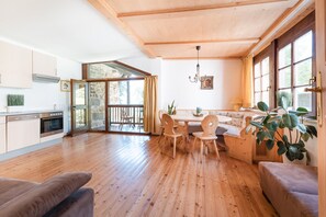Amplia sala de estar con piso de madera, una mesa de comedor con sillas, un sofá y un ventanal con cortinas.