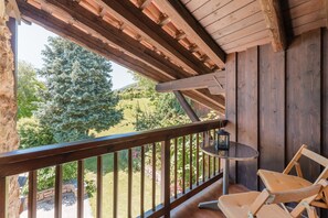 Un balcón de madera con vista a un jardín y árboles.