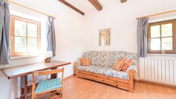Una habitación con piso de madera, un sofá con tapicería floral, una mesa de madera y una silla con cojín azul.