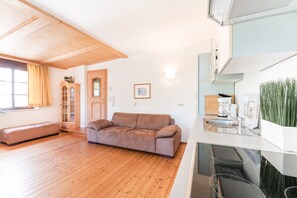 Una sala moderna con piso de madera, un sofá marrón, un mueble de madera y una zona de cocina con un lavamanos y una cafetera.
