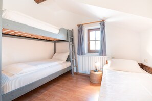 Habitación con literas, una escalera, ventana con cortinas, lámpara de noche y una cesta de mimbre.