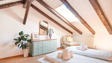 Un dormitorio con techo inclinado, vigas de madera, cómoda, espejo, planta, sofá y cama con toallas.