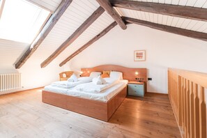 Un dormitorio con techo inclinado, vigas de madera, una cama con sábanas blancas, una mesita de noche y un cuadro en la pared.