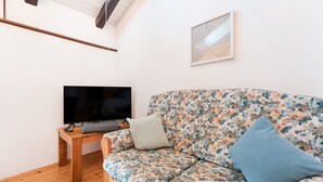Una sala de estar con piso de madera, un sofá tapizado con motivos florales, un televisor sobre un mueble de madera y un cuadro enmarcado en la pared.