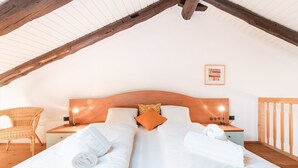 Un dormitorio con dos camas, cabeceras de madera, una silla de mimbre y un cuadro en la pared.