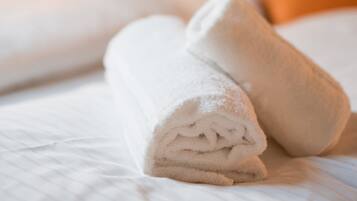 Un lit bien fait, avec du linge de lit blanc et deux serviettes enroulées.