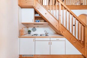 Une cuisine compacte avec un escalier en bois, des placards blancs, un évier et un petit plan de travail.