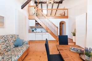 Una sala acogedora con una escalera de madera, un sofá con tapicería floral, una mesa de comedor con sillas y una zona de cocina.