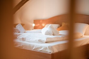 Una cama bien hecha con sábanas y toallas blancas, un cabecero de madera y una lámpara de noche.