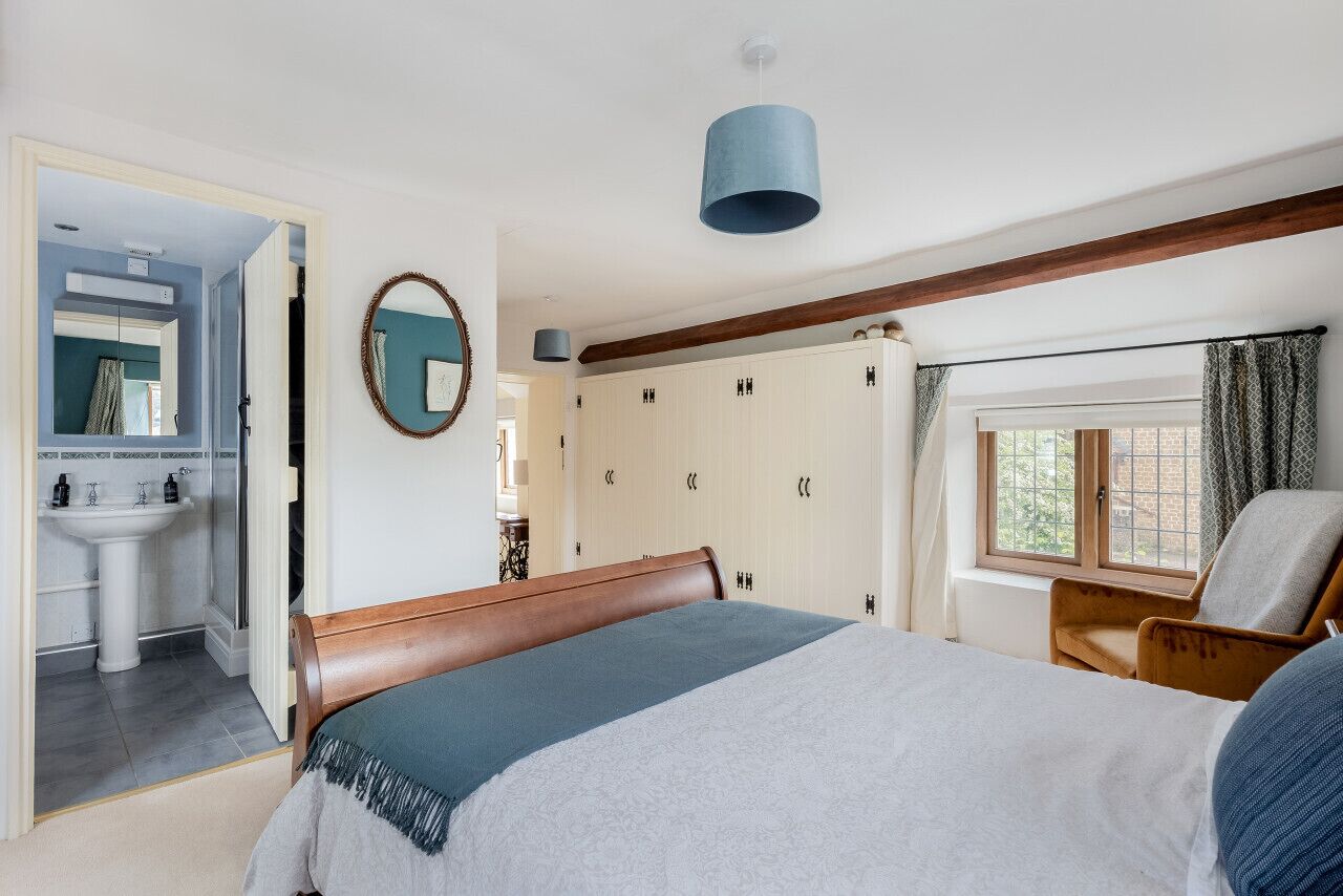 A bedroom with a bed, a chair, a wardrobe, a window, and a bathroom visible through an open door.