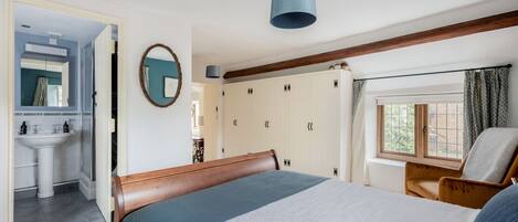 A bedroom with a bed, a chair, a wardrobe, a window, and a bathroom visible through an open door.