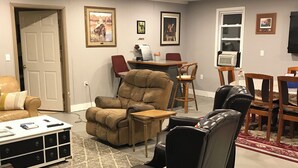 A living room with a beige sofa, a brown recliner, a black leather chair, and a dining area with a table and chairs. - HB Rustic Retreat - WGI - Book now for Race Weekend. A fun place for all ages. (Beaver Dams)