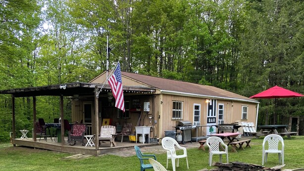 A rustic cabin with a covered porch, outdoor seating, and a barbecue area. - HB Rustic Retreat - WGI - Book now for Race Weekend. A fun place for all ages. (Beaver Dams)