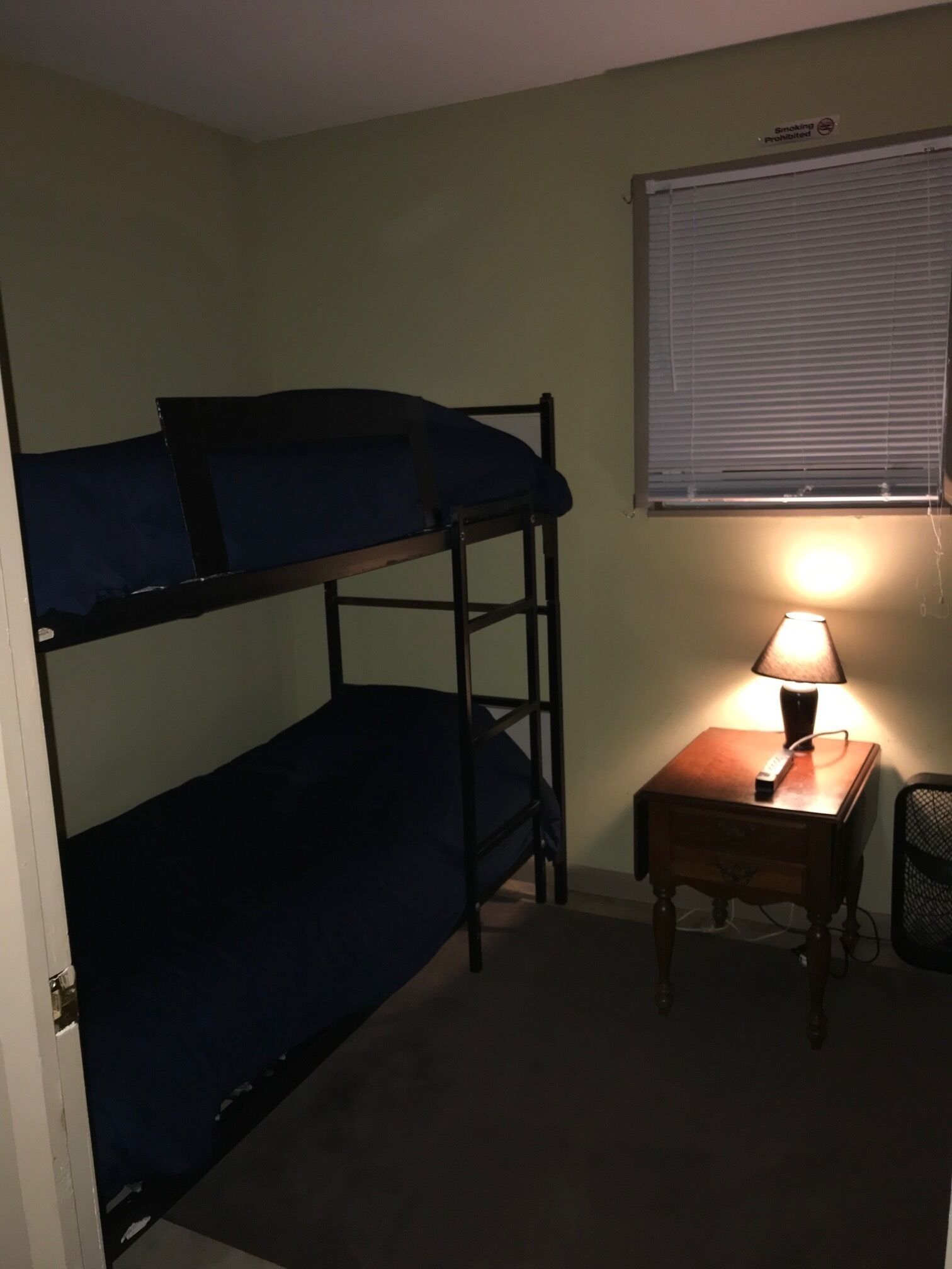 A bunk bed with a desk and lamp, a window with blinds, and a "Smoking Prohibited" sign.