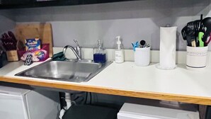 A kitchen with a sink, a white countertop, a trash bin, and a white appliance below. - HB Rustic Retreat - WGI - Book now for Race Weekend. A fun place for all ages. (Beaver Dams)