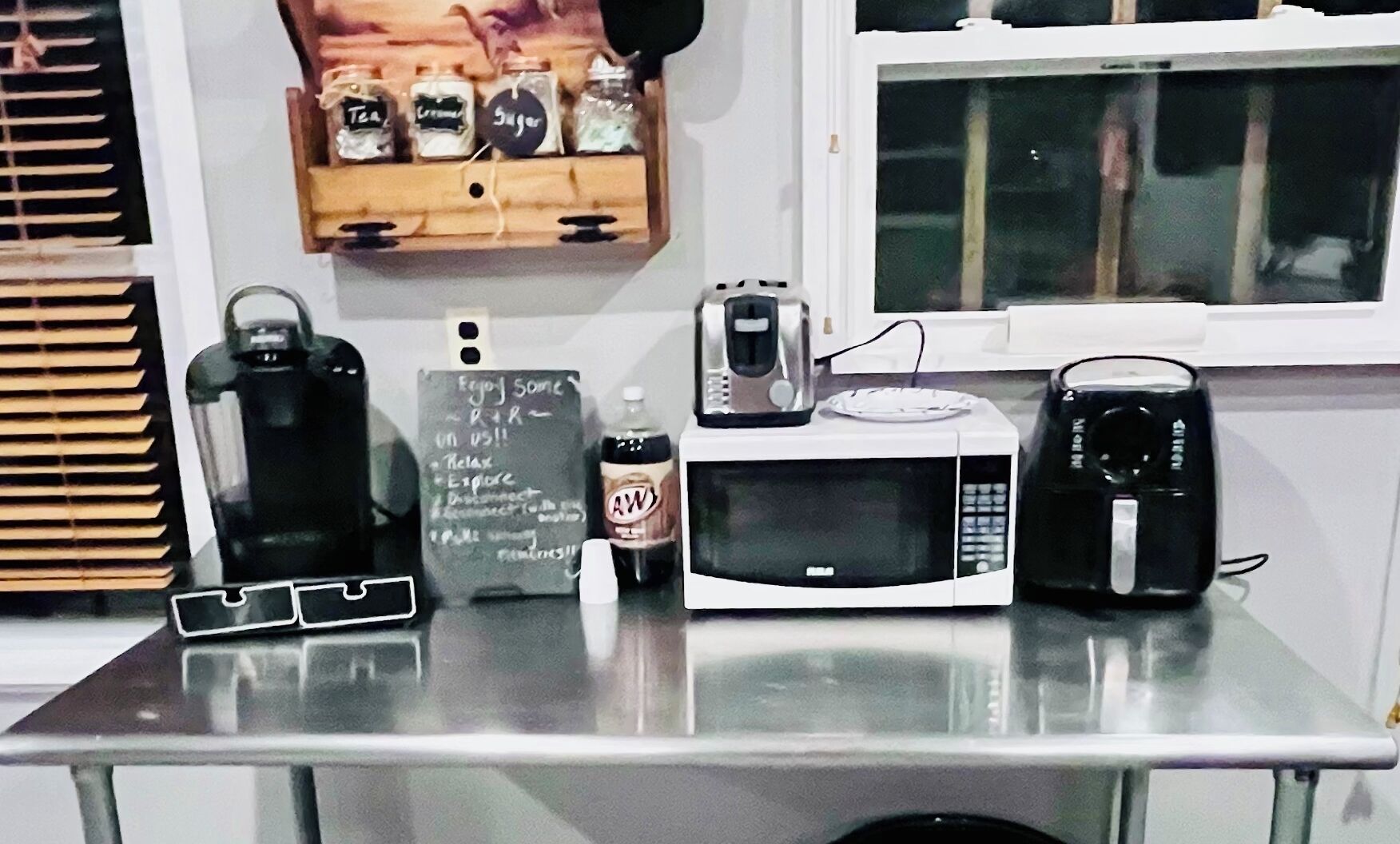 Una encimera de cocina con microondas, tostadora, hervidor, una botella de A&W root beer y una pizarra con notas escritas a mano.