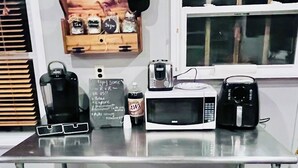 A kitchen counter with a microwave, a toaster, a kettle, a bottle of A&W root beer, and a chalkboard with handwritten notes. - HB Rustic Retreat - WGI - Book now for Race Weekend. A fun place for all ages. (Beaver Dams)