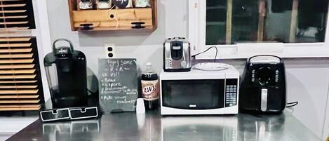 Una encimera de cocina con microondas, tostadora, hervidor, una botella de A&W root beer y una pizarra con notas escritas a mano.