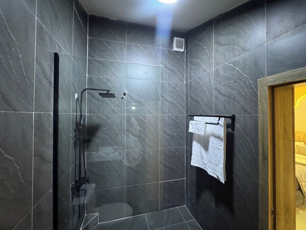 A modern bathroom with dark marble tiles, a glass-enclosed shower, and a towel rack.