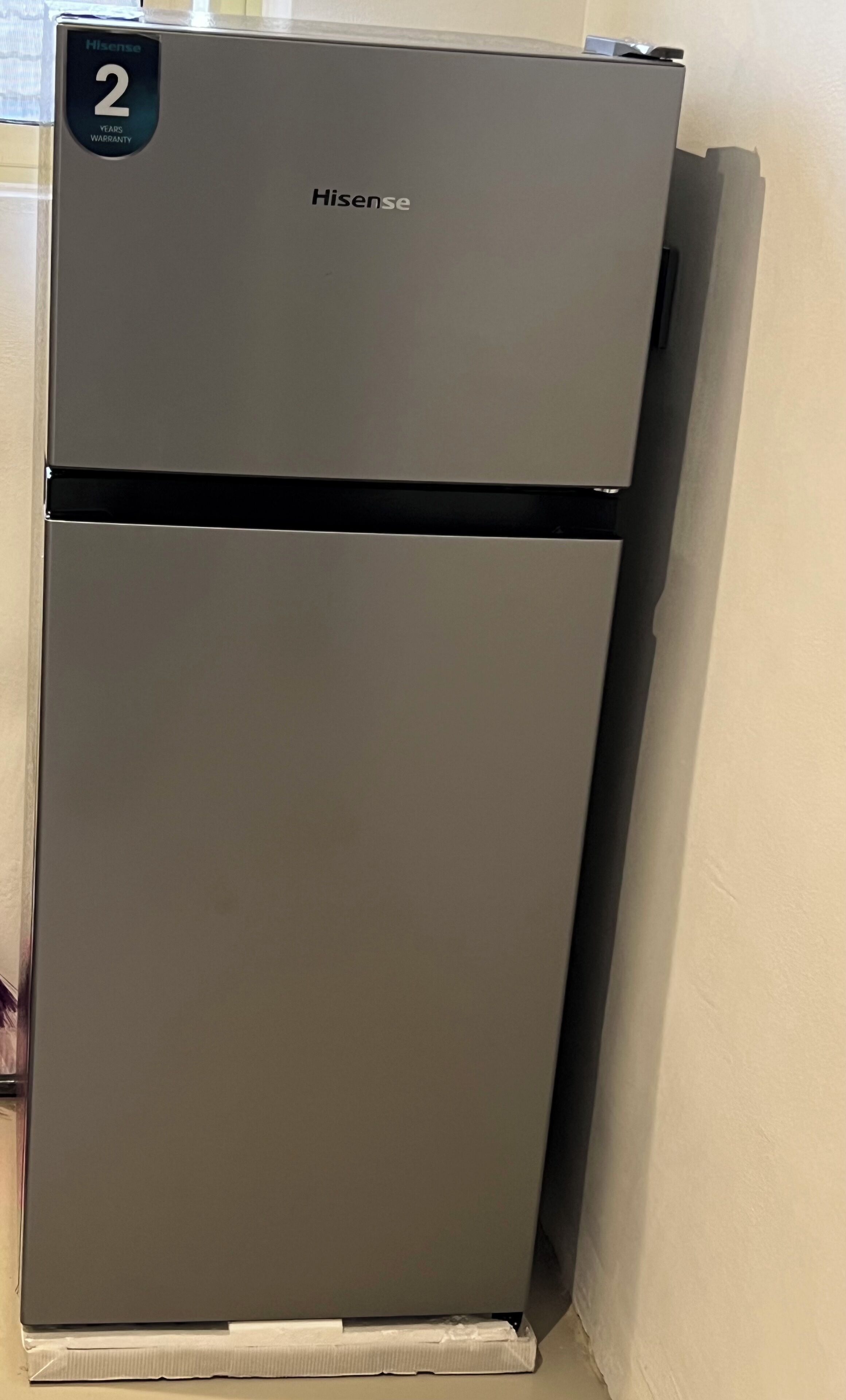 Un réfrigérateur Hisense avec un autocollant indiquant une garantie de deux ans, placé contre un mur uni.