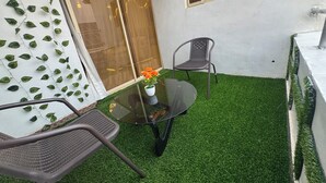 A patio with artificial grass, a glass table, two chairs, and a potted plant.