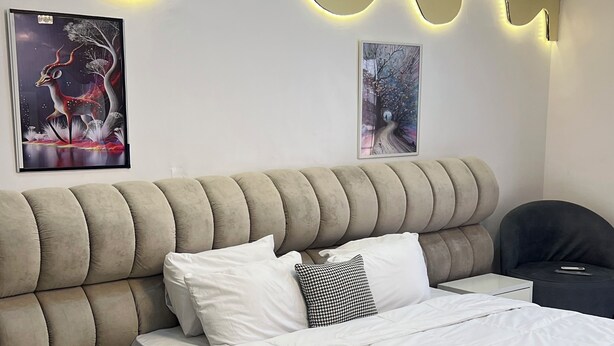 A modern bedroom with a tufted headboard, a large bed with white bedding, a bedside table, and two wall-mounted light fixtures.