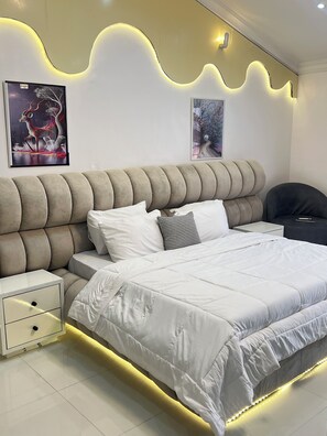A modern bedroom with a tufted headboard, a large bed with white bedding, a bedside table, and two wall-mounted light fixtures.