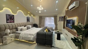 A modern bedroom with a large bed, a sofa, a TV, and a decorative plant.