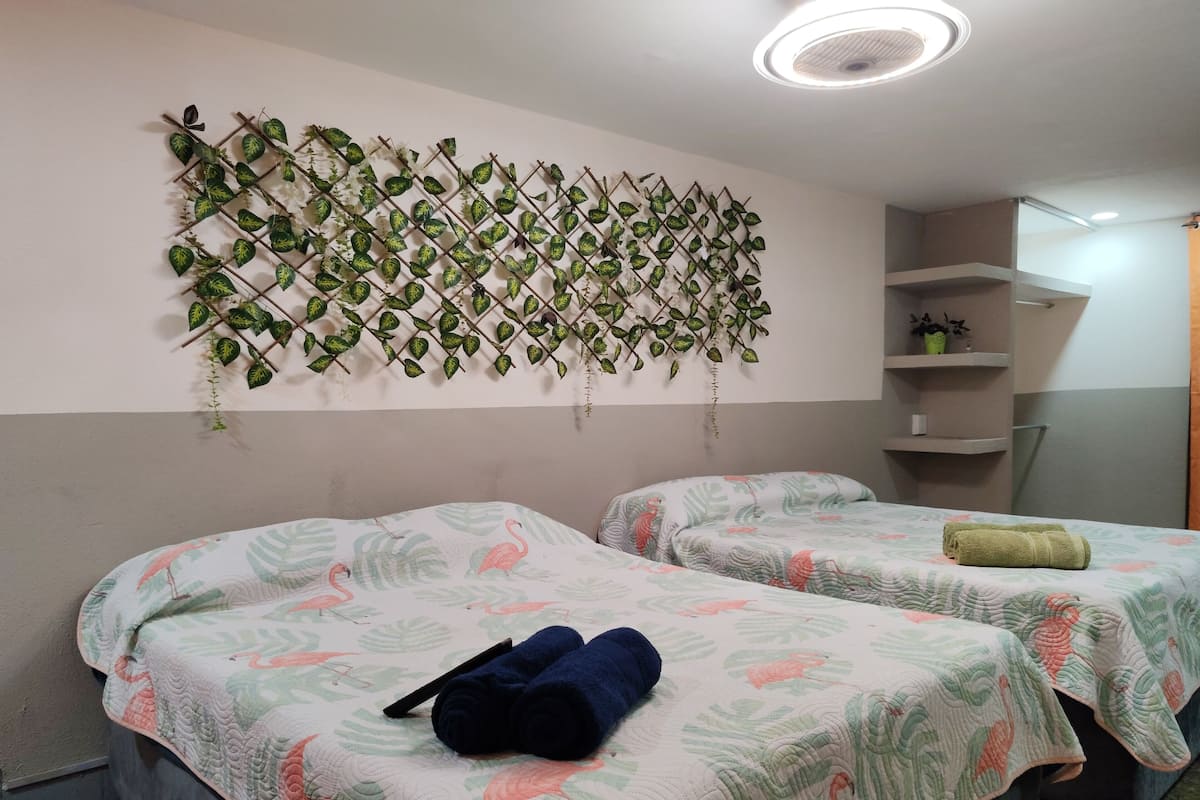 Una stanza con due letti, ognuno con una coperta a motivi floreali e un asciugamano arrotolato su un letto. Sopra i letti, una decorazione a pianta fissata al muro.