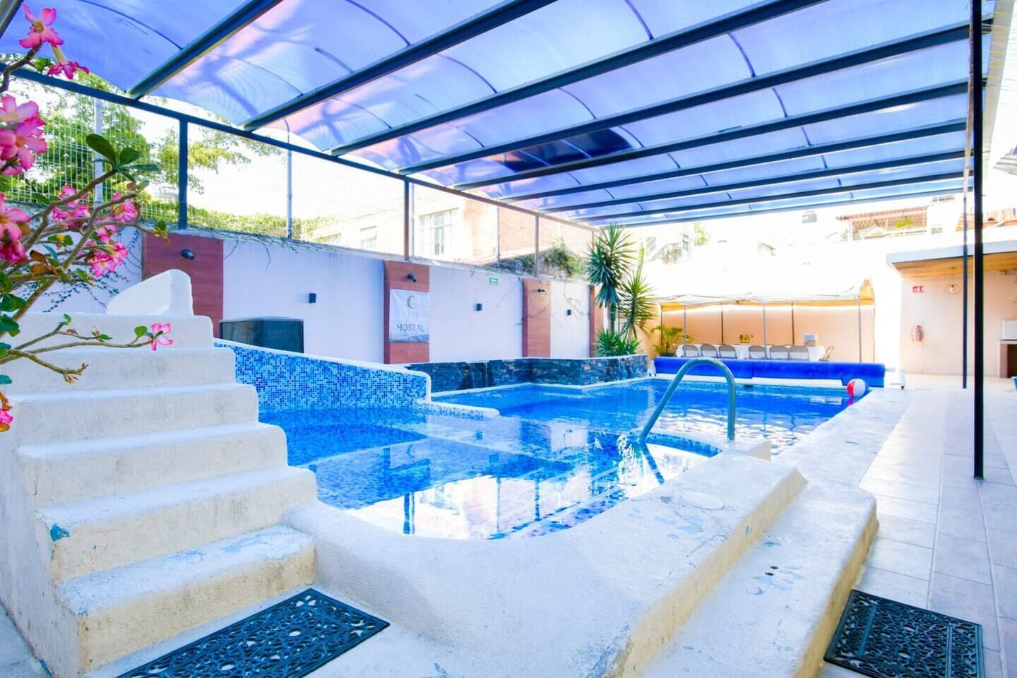 Una piscina interior con agua cristalina, un área techada con un toldo azul y una escalera que lleva a la piscina.