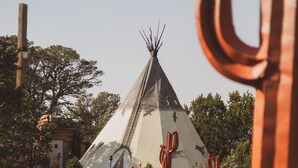 En stor tipi med en stige, omgivet af træer og en græsplæne.