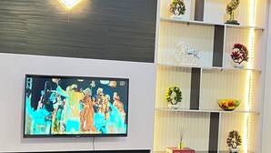 A modern living room with a flat-screen TV mounted on the wall, a white entertainment unit below, and decorative shelves with various items. - Serene environment perfect for a pri8 short or long stay.Beach,bar n mall nearby (Eti-Osa)