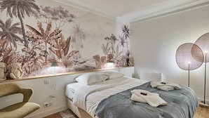 A bedroom with a bed, a chair, a wall mural, and a floor lamp. - Modern Apartment - Eiffel Tower Trocadero Place (Paris)