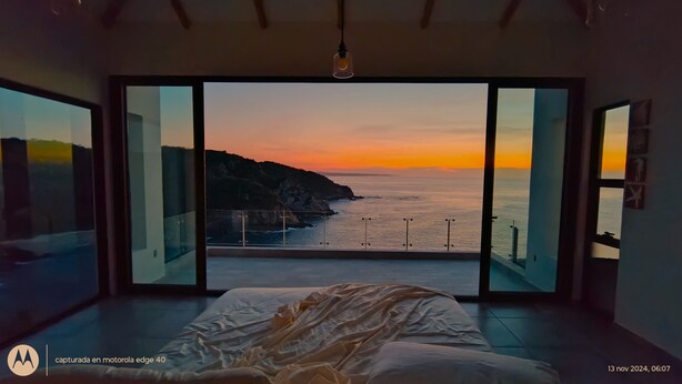A bedroom with a large sliding glass door leading to a balcony with a view of the sea and cliffs at sunset. - UNIQUE BEACH HOUSE CASA DI LUCA WITH STUNNING VIEW (Puerto Ángel)