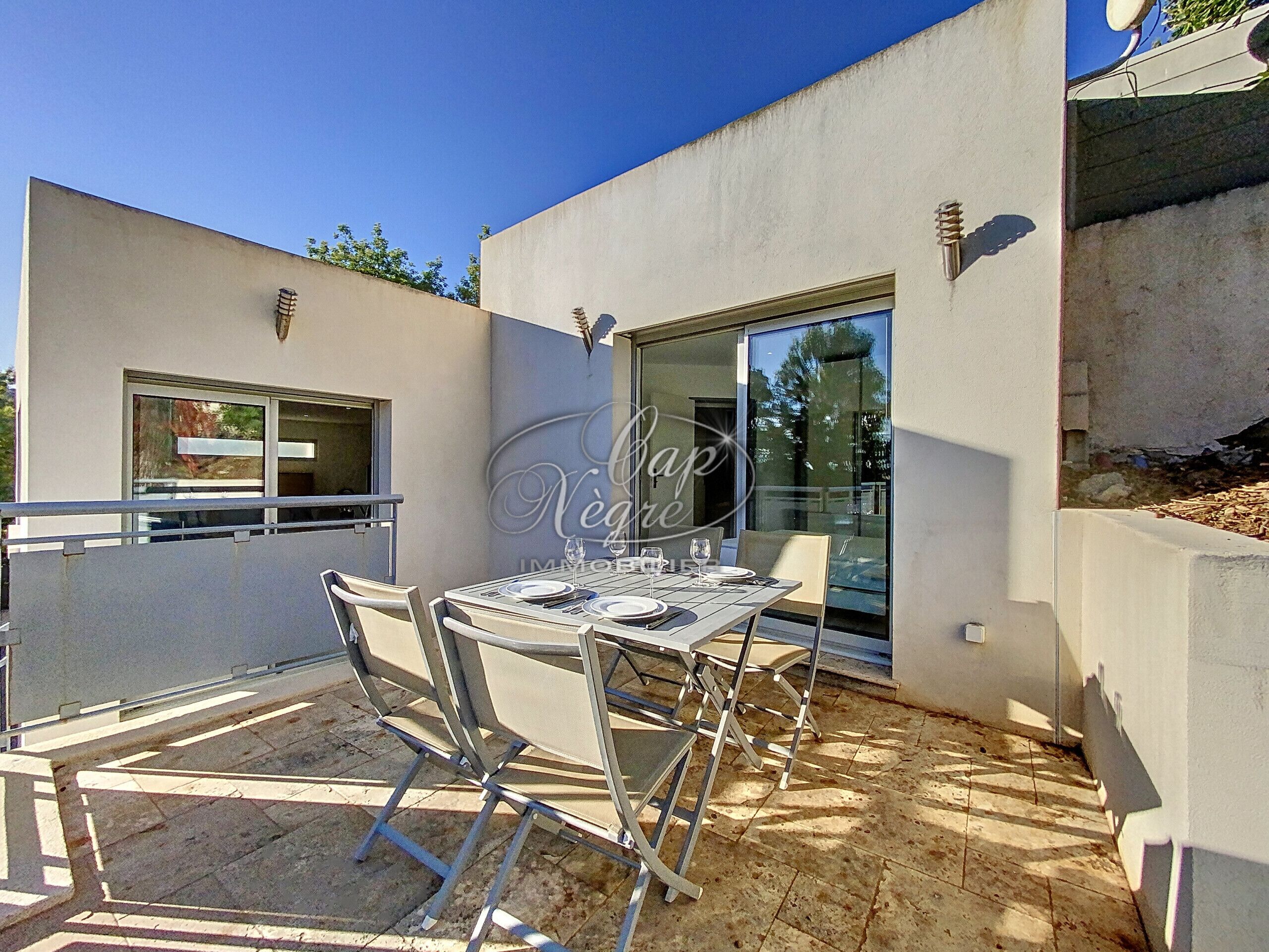 An outdoor patio with a table set for two, a glass door leading to a covered area, and a window on the adjacent wall.