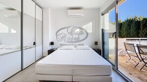 A modern bedroom with a large bed, a glass door leading to an outdoor area, and a wall-mounted air conditioning unit. - Modern house for 4 people close to Cavalière beach in Le Lavandou (Le Lavandou)