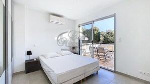 A bedroom with a bed, a nightstand, and a sliding glass door leading to an outdoor patio with chairs and a table. - Modern house for 4 people close to Cavalière beach in Le Lavandou (Le Lavandou)