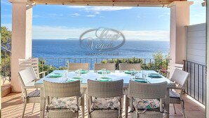 Un espacio exterior cubierto para comer con muebles de mimbre y una mesa preparada para cuatro, con vista a un paisaje marino.