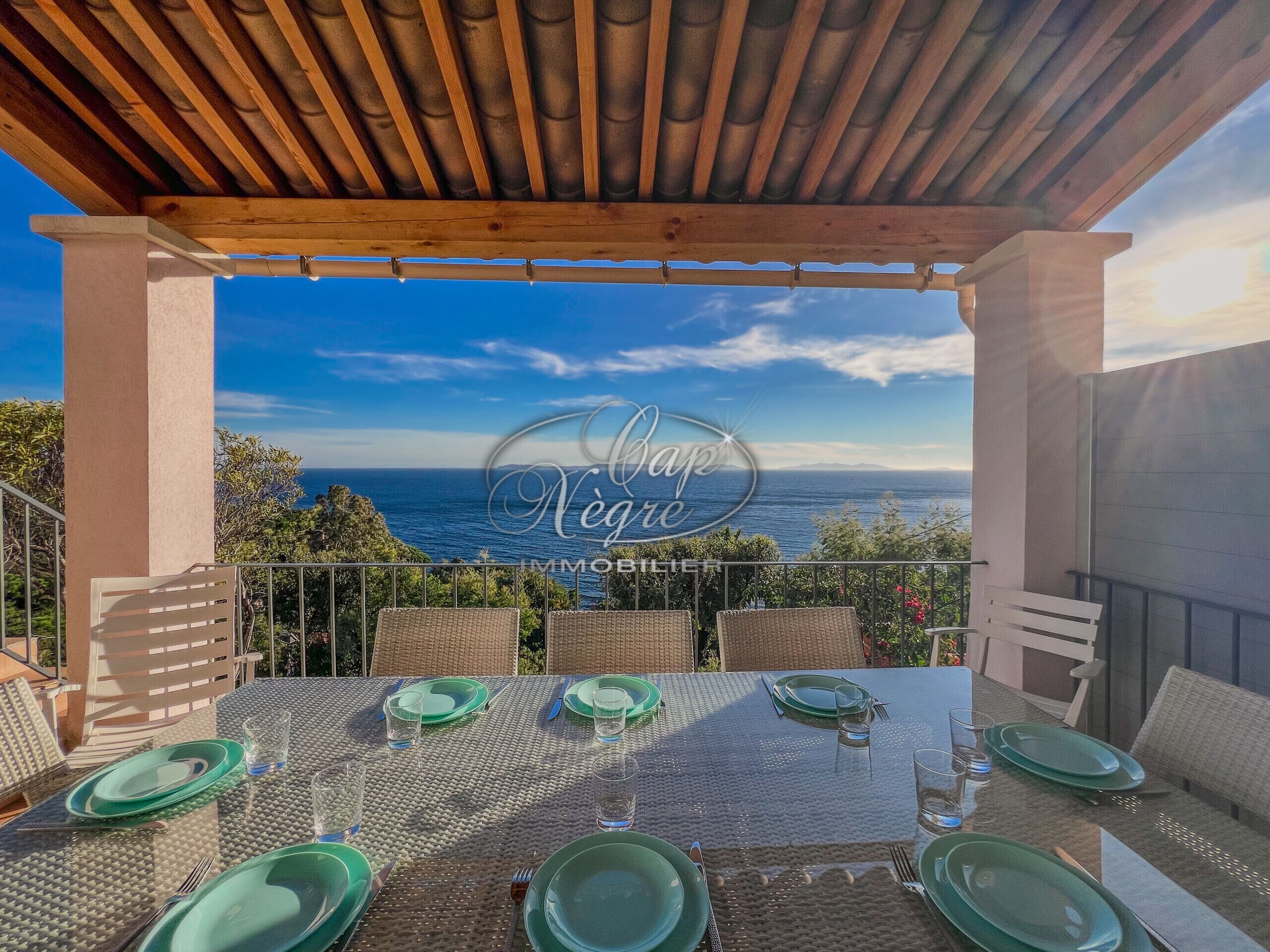 A covered outdoor dining area with a view of the sea, featuring a table set with green plates and glasses.