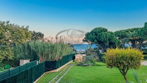 A well-maintained garden with a pathway leading to a beach, surrounded by lush greenery and palm trees.