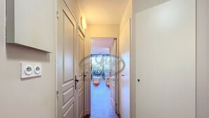 A narrow hallway with white doors, a light switch, and a power outlet on the wall.
