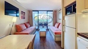 A compact living space with a sofa set, a dining table, and a kitchen area with appliances.