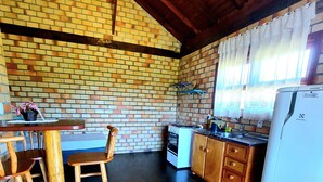 Una cocina con pared de ladrillo, techo de madera y un refrigerador blanco.