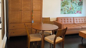 A room with a wooden cabinet, a round table with chairs, a sofa, and a wall-mounted painting.