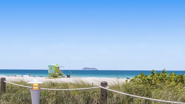 A beach with a lifeguard tower, a rope barrier, and a ship in the distance.