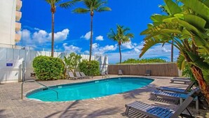 A swimming pool with lounge chairs, palm trees, and a clear blue sky.