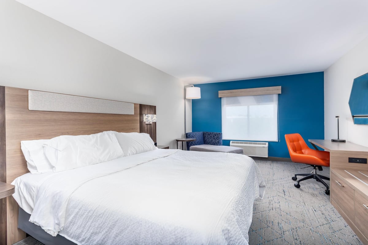 A hotel room with a bed, a desk, an orange chair, a blue wall, and a window.